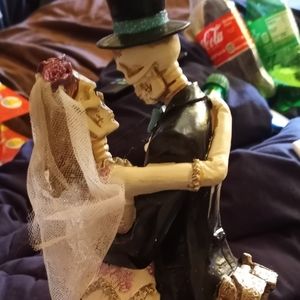 Bride and groom as skeletons slow dancing in front of a gravestone tall statue